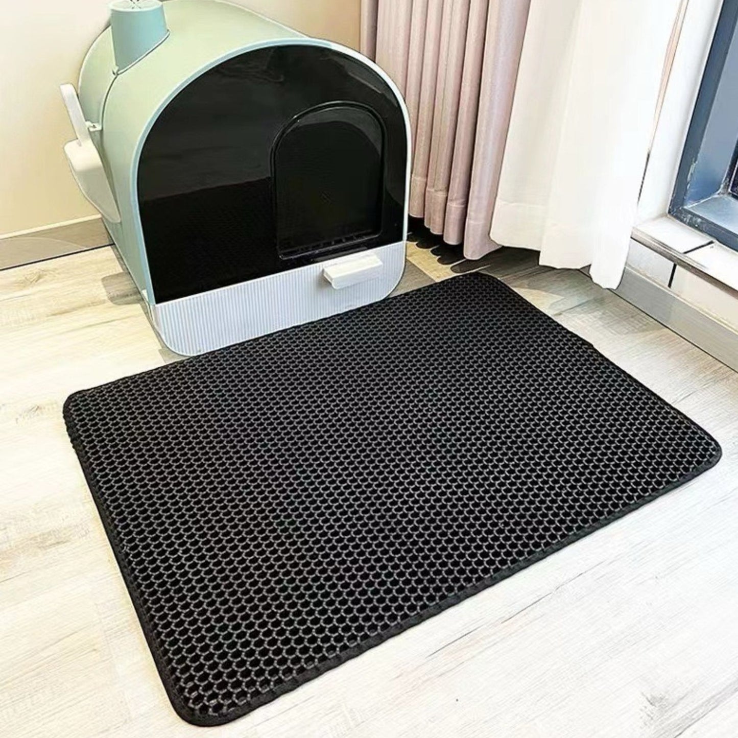 Black hexagonal mat in front of a cat litter box on a light wood floor.