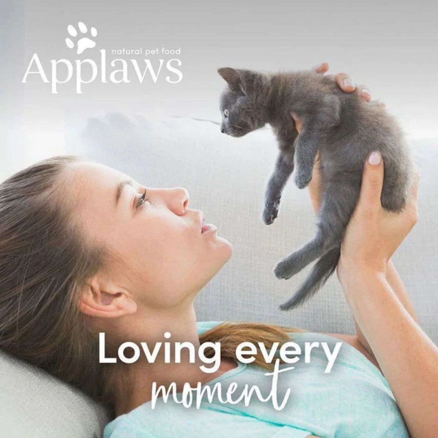 Woman holding a gray kitten with 'Applaws' logo and text 'Loving every moment' on a light background