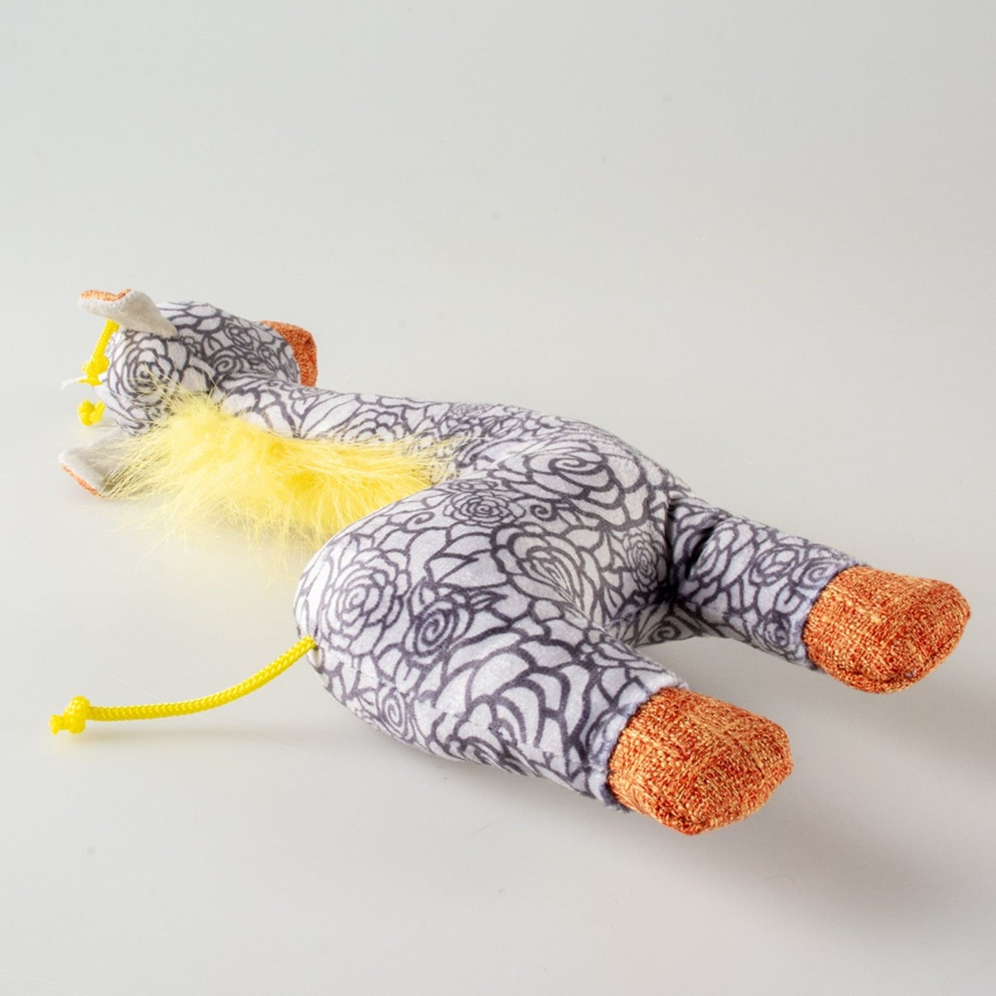 Toy shaped girrafe with a patterned body and orange feet on a light grey background
