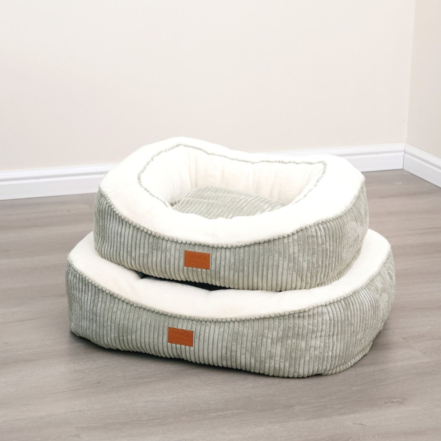 Two pet beds stacked on a wooden floor with a neutral background