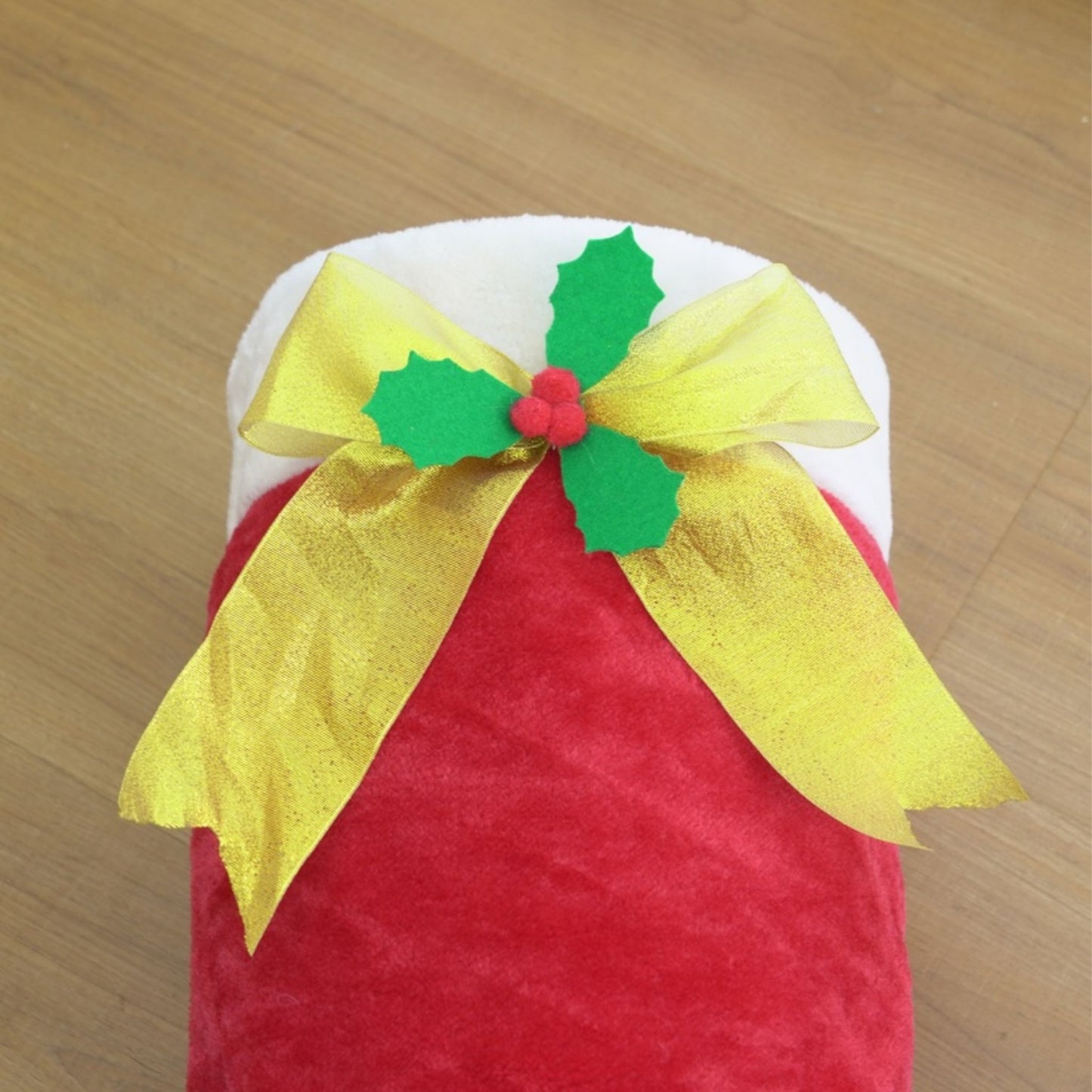 Red container with a yellow bow and green holly leaves on a wooden surface