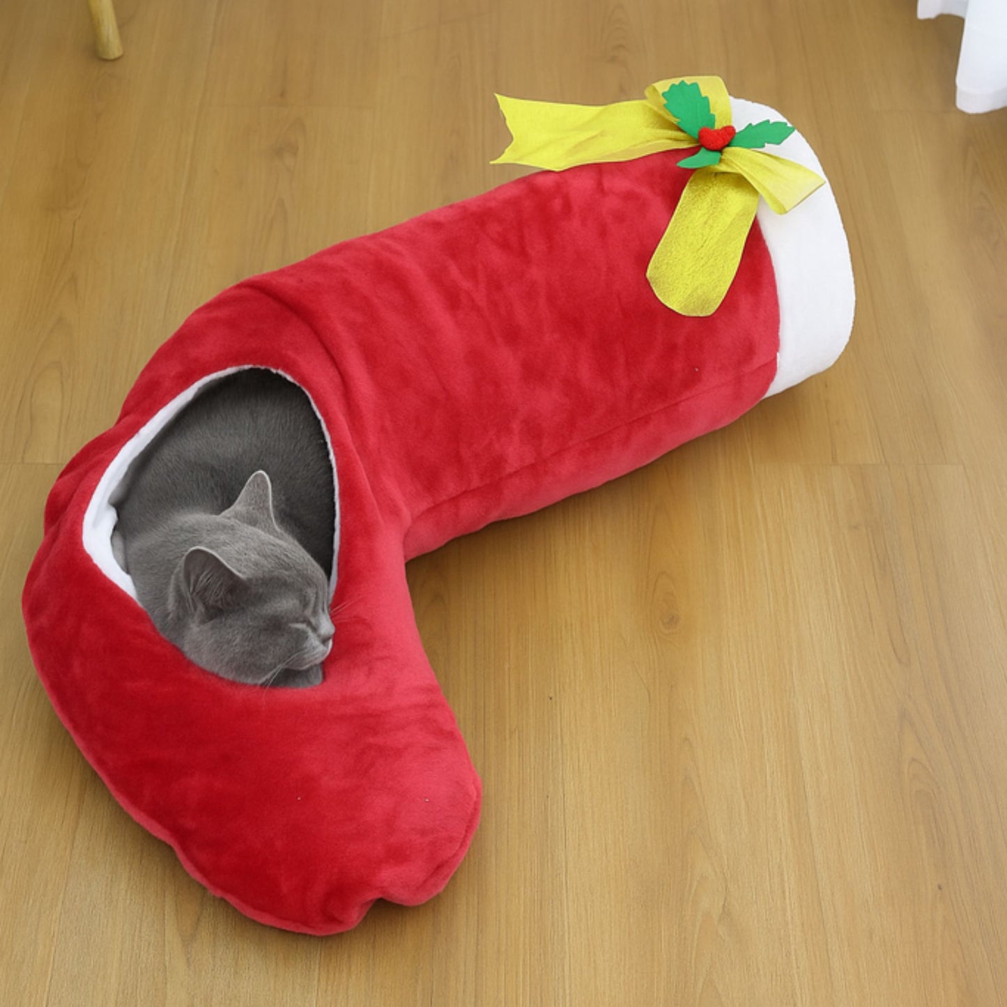 Red pet bed shaped like a strawberry with a yellow bow on a wooden floor.