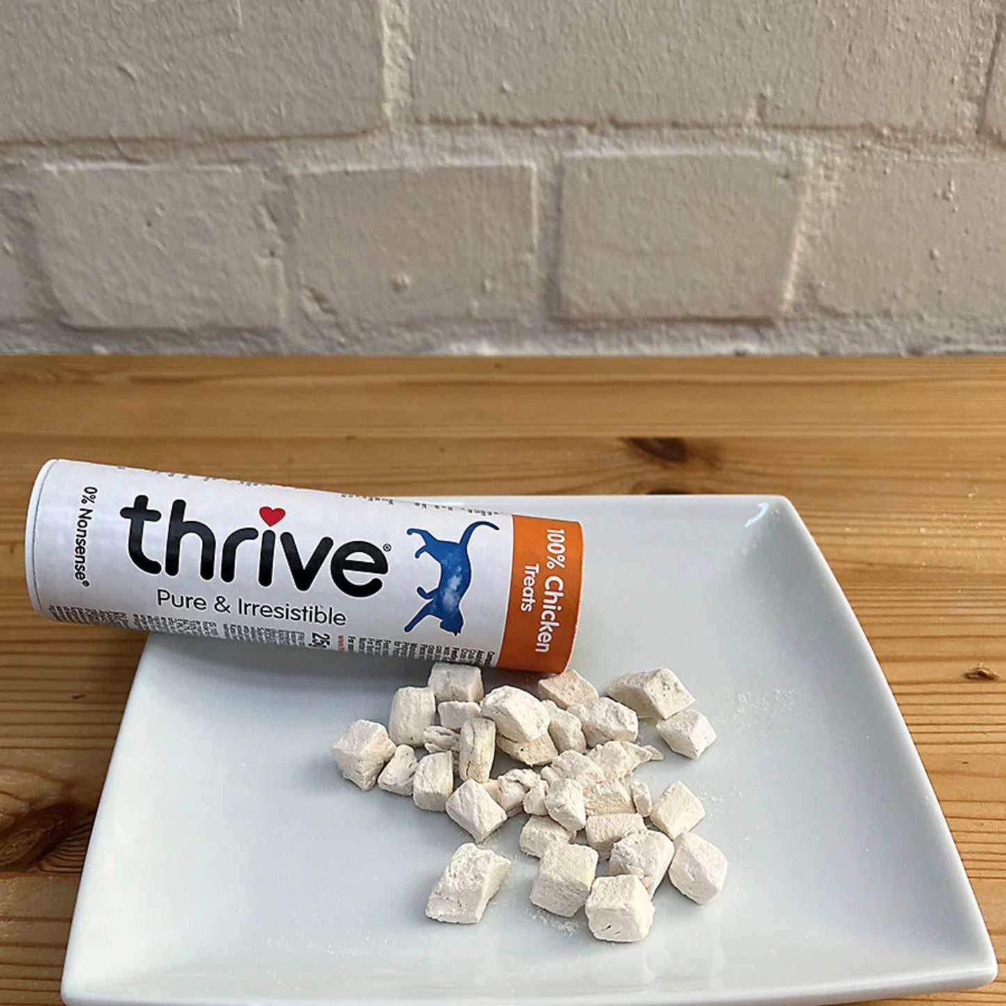 Thrive dog treat packaging with treats on a white plate against a brick wall background