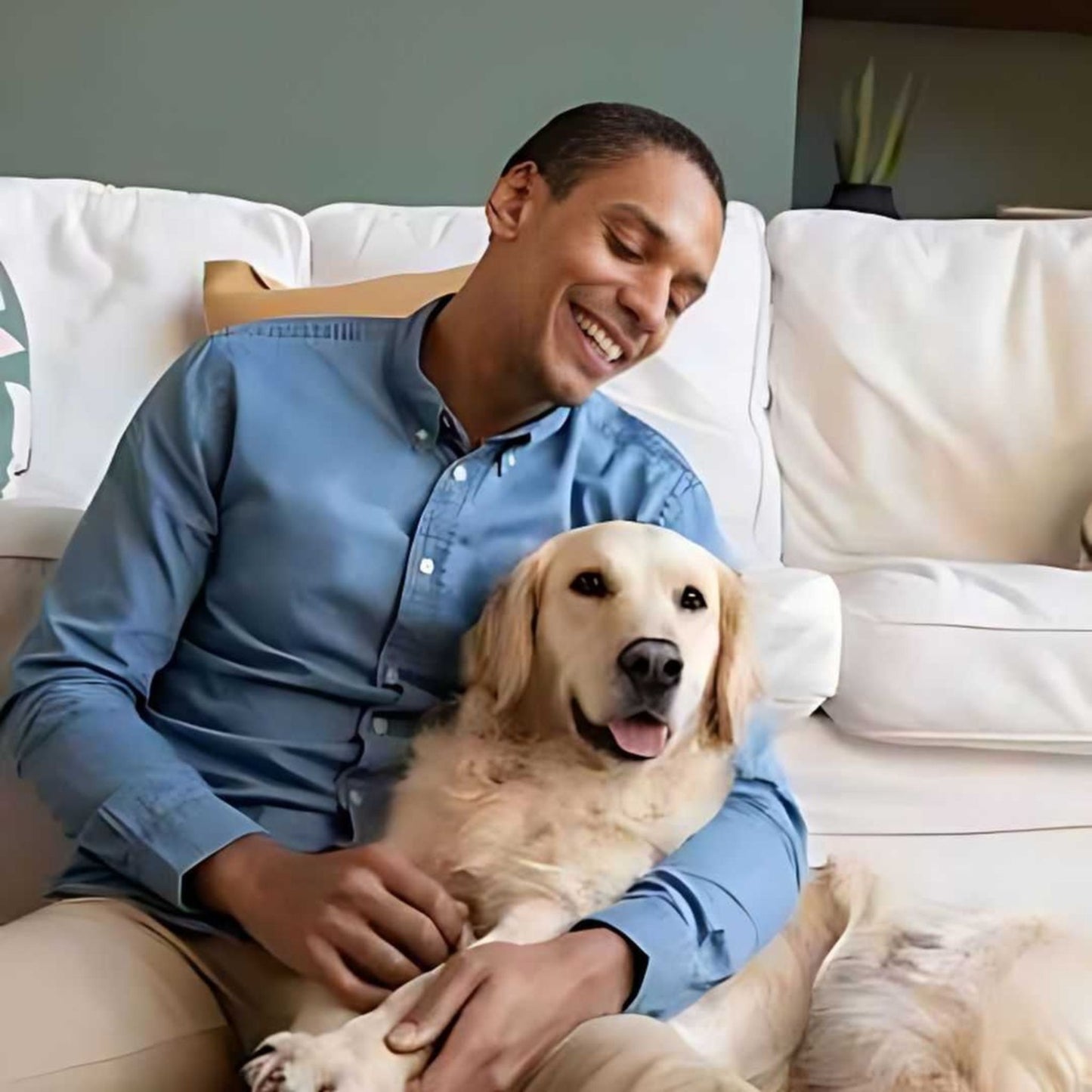 Man sitting on a couch with a golden retriever dog, smiling.